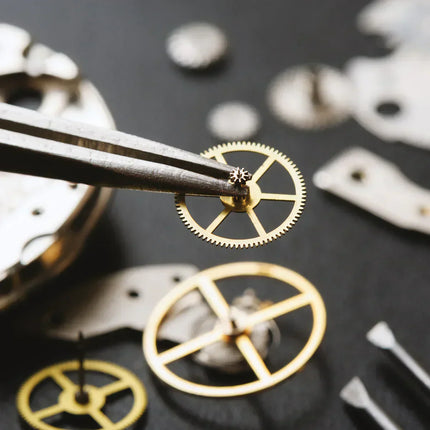 Close-up of a Swiss watchmaker holding a gold watch gear being held with tweezers with a black background