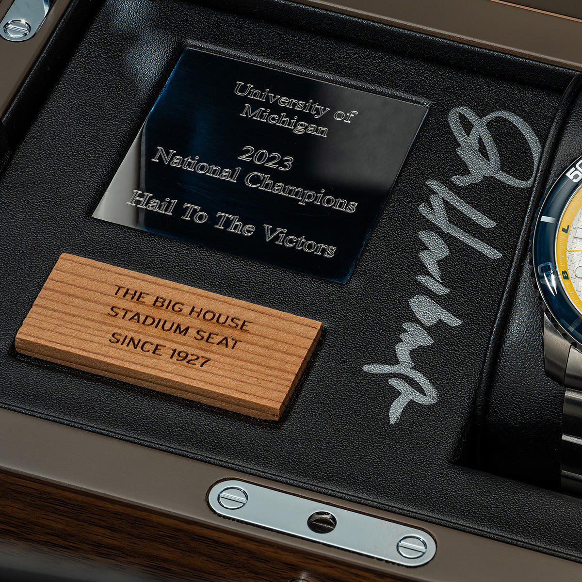 Close up view of the 2023 Michigan National Champions Jim Harbaugh autographed display box with the Odysseus Swiss made automatic watch and a piece of wood from The Big House stadium seats originally installed in 1927.