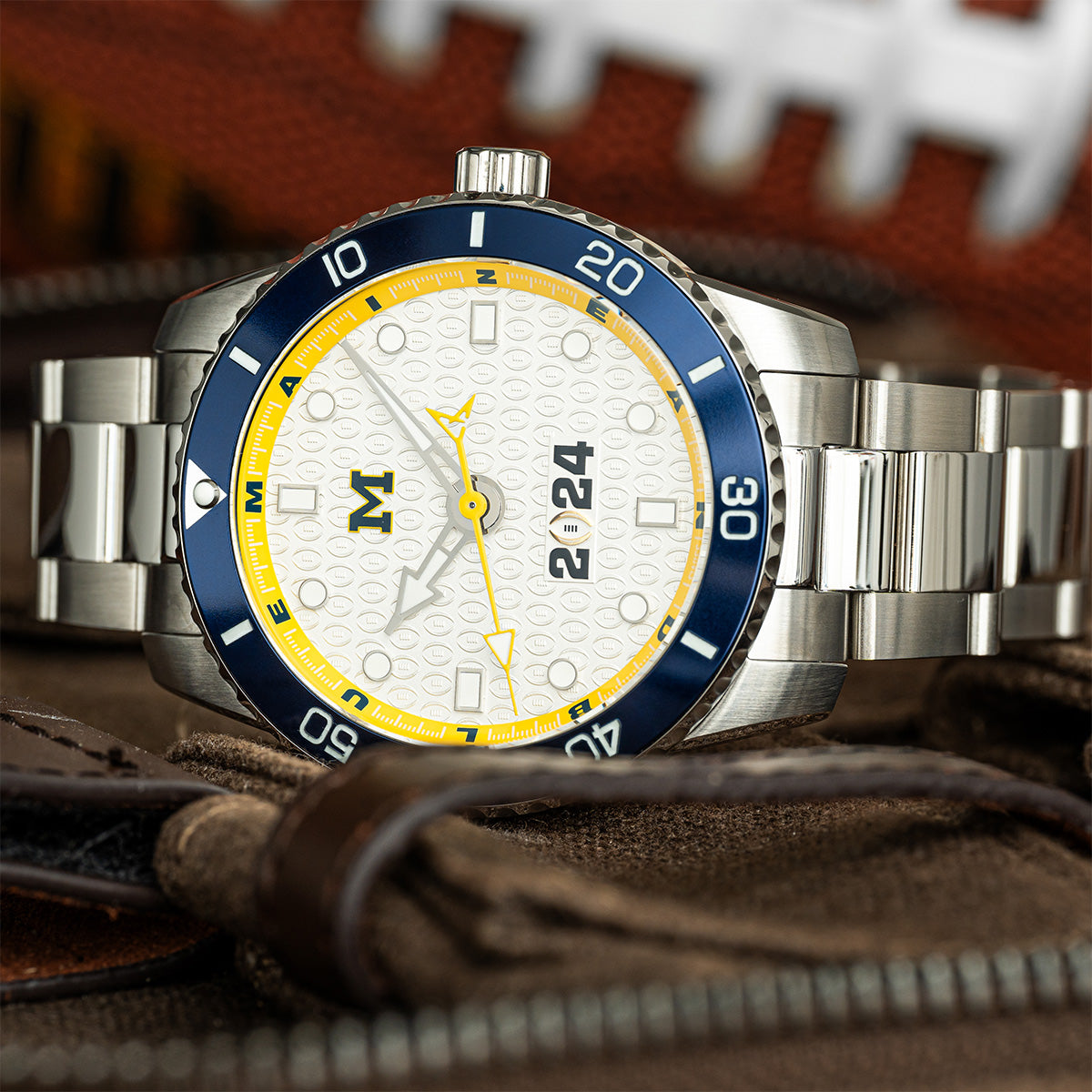 CFP 2024 Michigan Wolverines Odysseus swiss made automatic watch. Stainless steel bracelet strap on its side on a table.